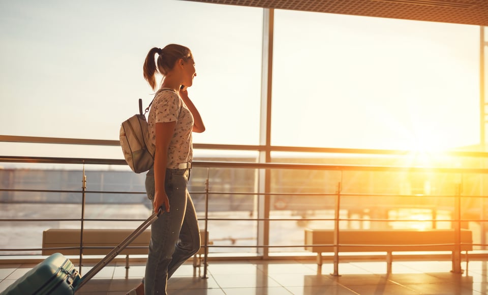 Jeune femme au téléphone à la fenêtre de l'aéroport avec des bagages